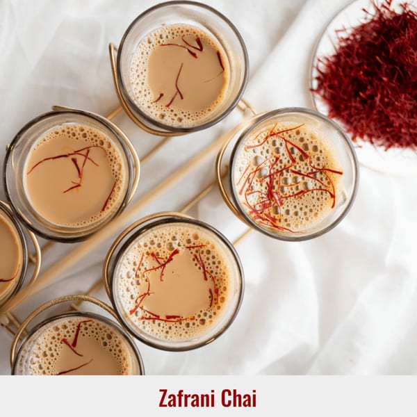 Overhead view of six glasses of frothy Zafrani Chai, garnished with saffron threads, on a gold tray.