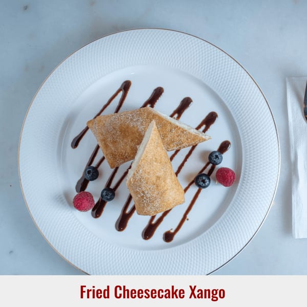 Fried Cheesecake Xango dessert on a white plate with chocolate drizzle, blueberries, and raspberries.