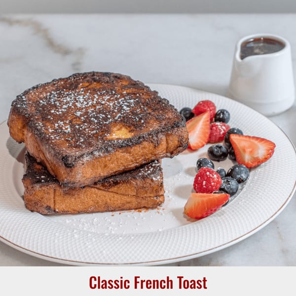 Two slices of French toast dusted with powdered sugar, served with fresh berries and syrup.
