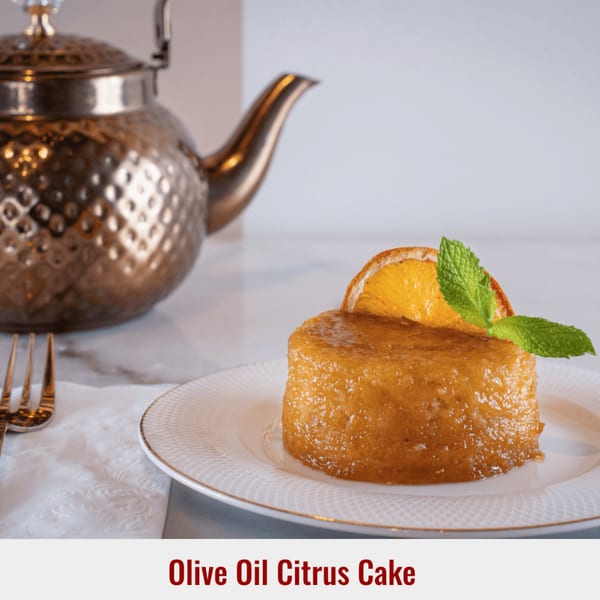 Olive Oil Citrus Cake on a white plate with an orange slice, mint, and a teapot.