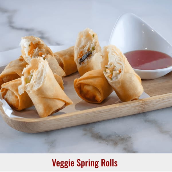 Golden-brown veggie spring rolls, some cut open to show filling, served with dipping sauce on a wooden tray.
