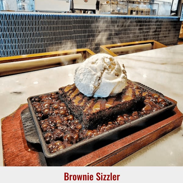 Sizzling brownie with vanilla ice cream and chocolate sauce on a wooden tray at Dessert Avenue.