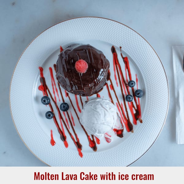 Molten lava cake with a raspberry, vanilla ice cream, blueberries, and red syrup on a white plate.