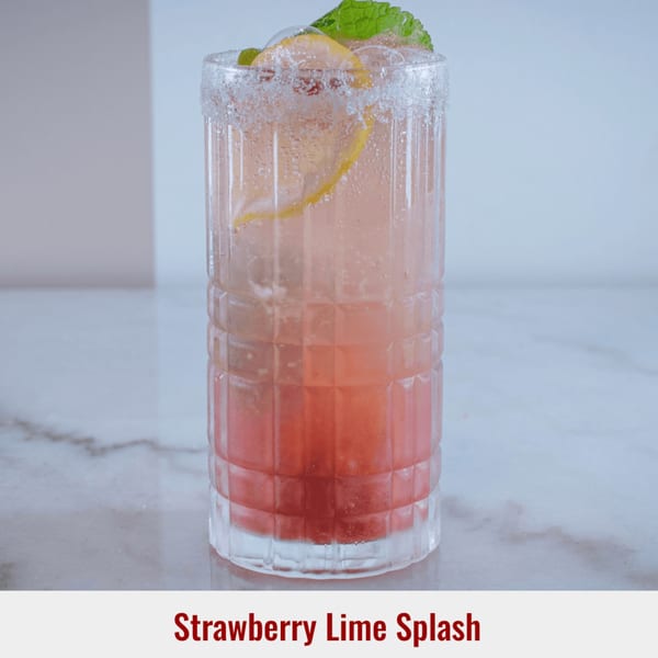 A Strawberry Lime Splash drink in a tall glass with a sugar rim, garnished with mint and lemon.